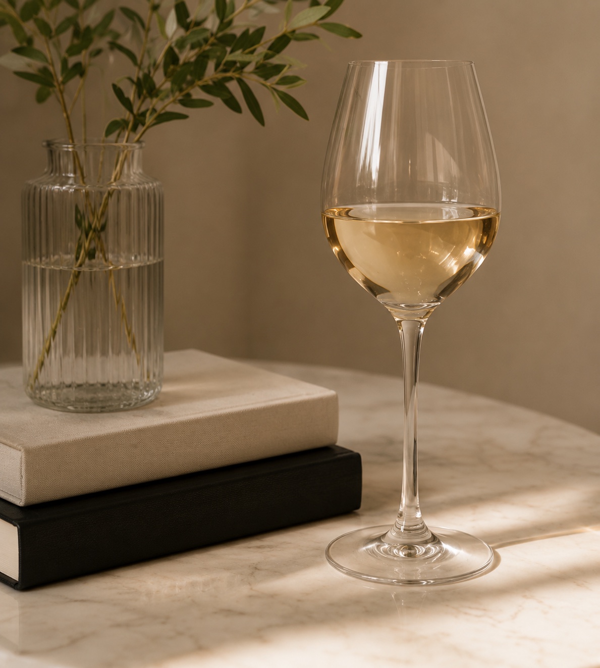 A glass of white wine beside stacked books and a leafy branch