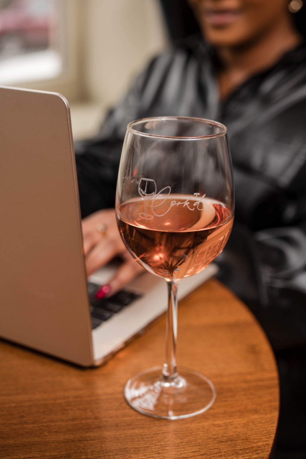 A glass of Cork’d rose beside an open laptop on a cafe table